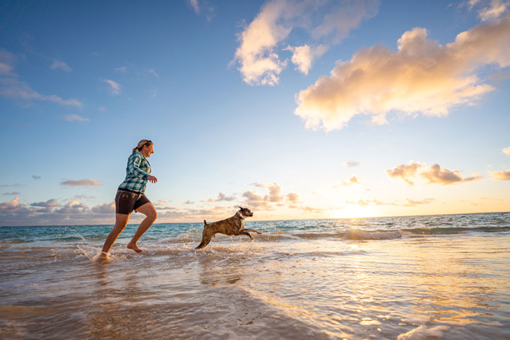 Active woman enjoying a healthy lifestyle, enjoying chasing her dog on a sunny beach, embodying vitality and weight loss success.