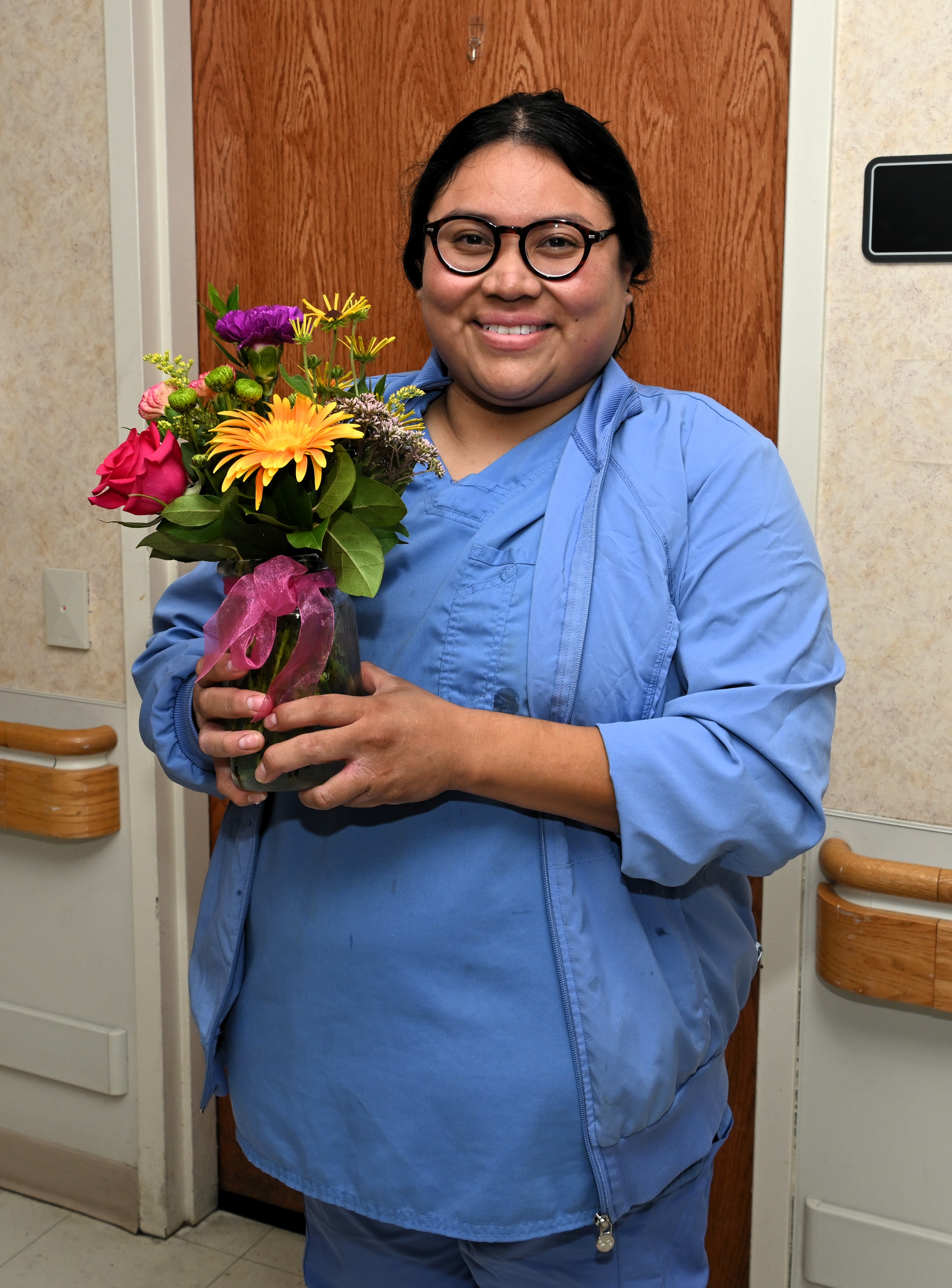 a woman in blue scrubs holding flowers in front of her