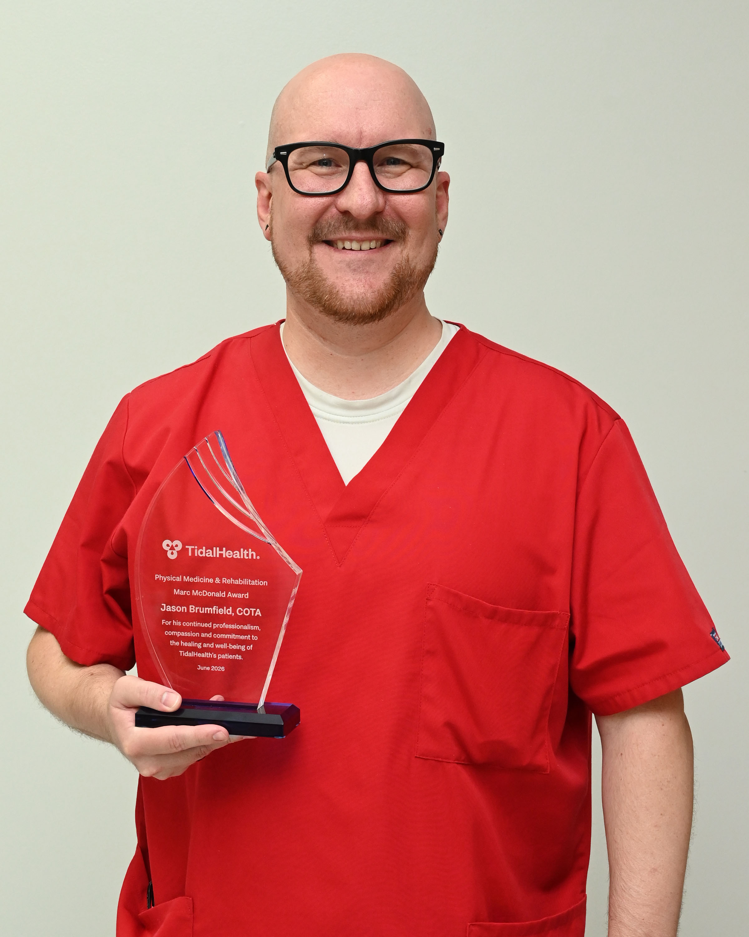 a man in red scrubs and glasses holding an award