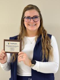 A woman in a white shirt with glasses holding her award next to her