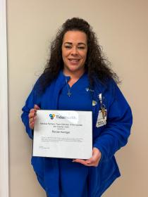 a woman in blue scrubs holding a certificate in front of her