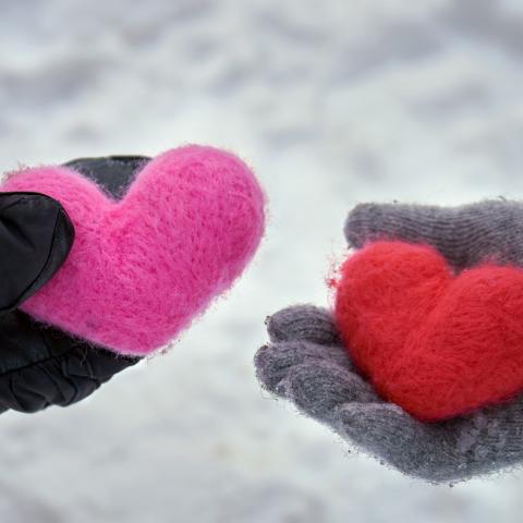 Two hands wearing gloves and holding yarn hearts in the winter snow