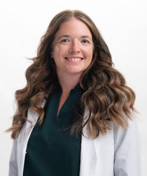 a woman in a black scrubs and white coat, with long hair posing for a portrait