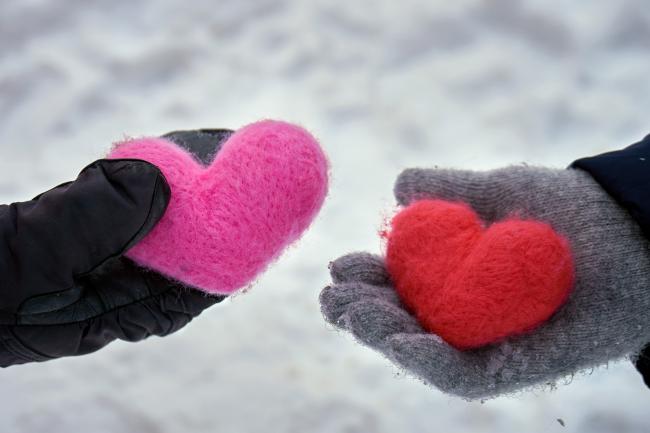 Two hands wearing gloves and holding yarn hearts in the winter snow