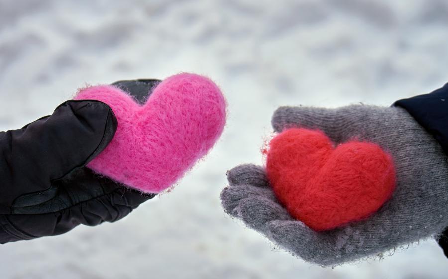 Two hands wearing gloves and holding yarn hearts in the winter snow
