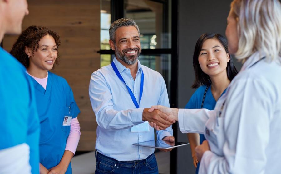 5 practitioners greet each other, shaking hands and smiling wearing blue